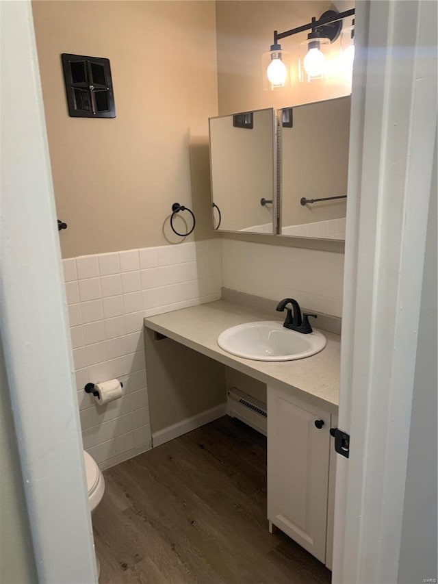 bathroom featuring toilet, wood finished floors, vanity, a baseboard heating unit, and tile walls