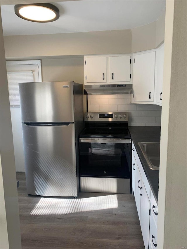 kitchen with under cabinet range hood, stainless steel appliances, a sink, white cabinetry, and dark countertops