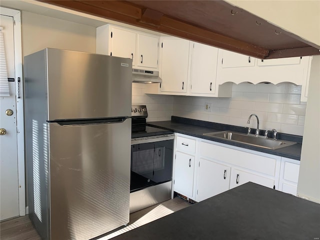 kitchen with under cabinet range hood, range with electric cooktop, a sink, freestanding refrigerator, and dark countertops