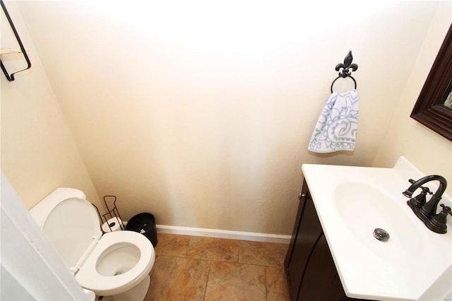 half bathroom featuring toilet, baseboards, and vanity