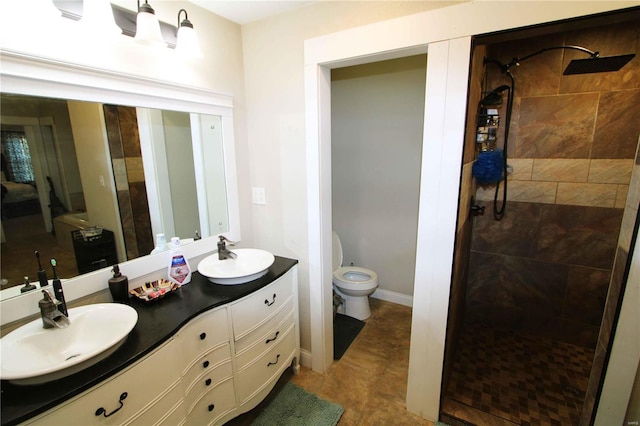 full bathroom featuring double vanity, tiled shower, a sink, and toilet