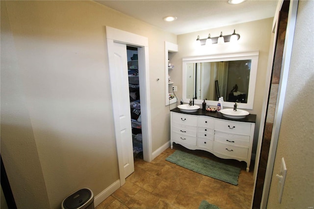 bathroom with recessed lighting, a sink, baseboards, double vanity, and a walk in closet