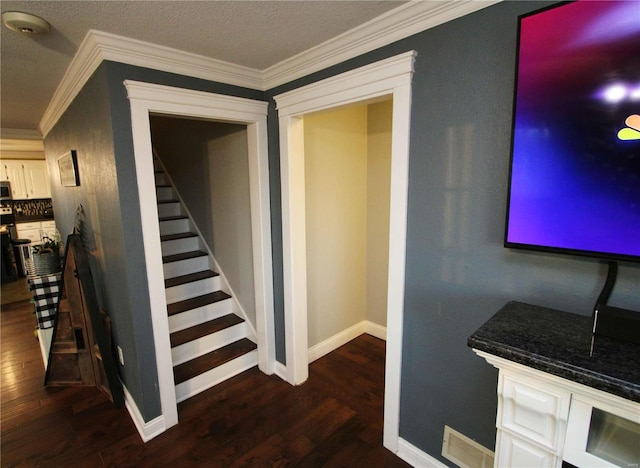 stairway with baseboards, wood finished floors, visible vents, and crown molding