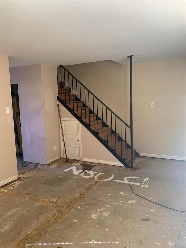 unfurnished living room featuring stairway and baseboards