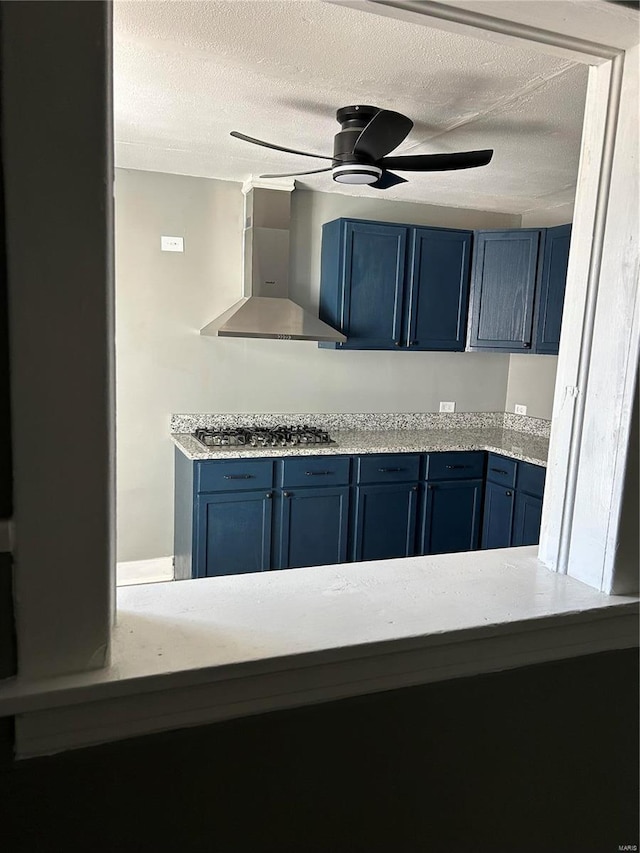 kitchen featuring blue cabinets, wall chimney exhaust hood, stainless steel gas stovetop, and ceiling fan