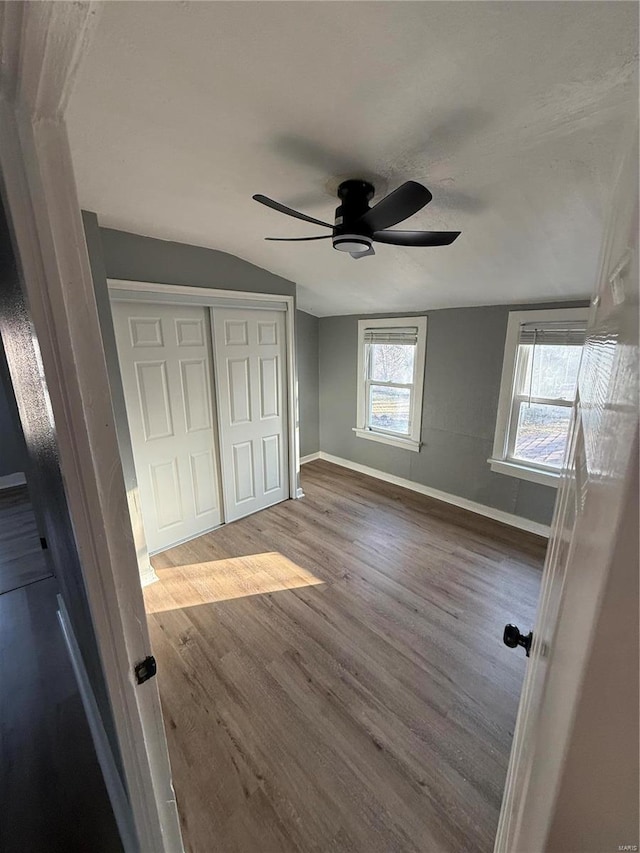 unfurnished bedroom with lofted ceiling, a closet, a ceiling fan, wood finished floors, and baseboards