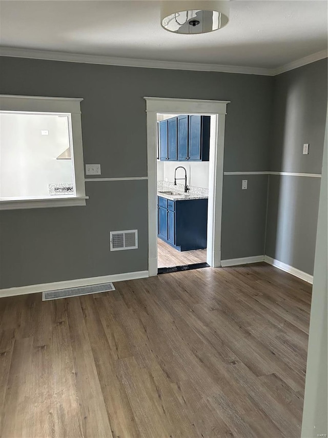 unfurnished room featuring visible vents, wood finished floors, a sink, and ornamental molding