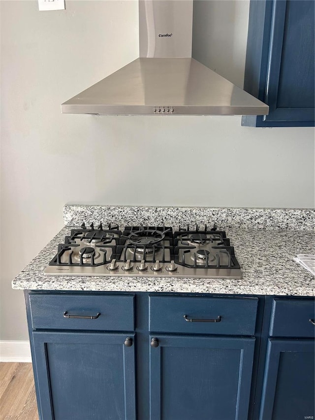 kitchen featuring stainless steel gas cooktop, wall chimney exhaust hood, blue cabinetry, and light wood-type flooring