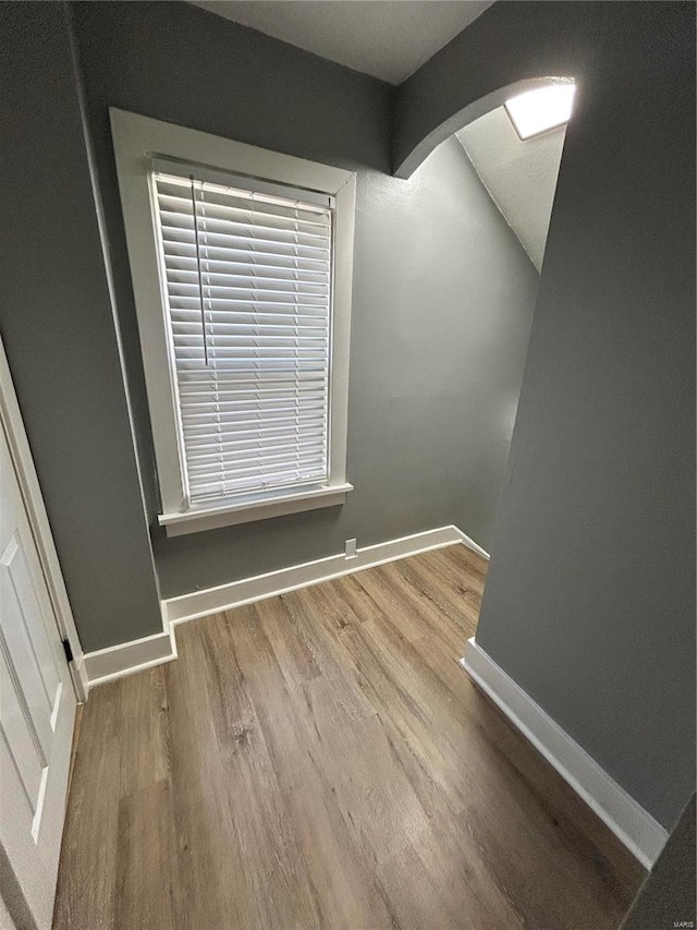 unfurnished room featuring arched walkways, baseboards, and wood finished floors