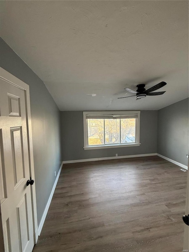 unfurnished room featuring a ceiling fan, lofted ceiling, dark wood-style flooring, and baseboards