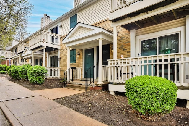 entrance to property with covered porch, a chimney, and brick siding