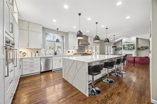 kitchen featuring stainless steel appliances, dark wood finished floors, wall chimney exhaust hood, and tasteful backsplash