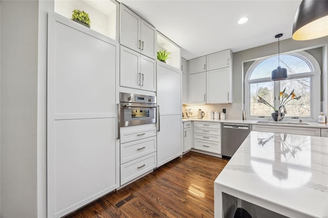 kitchen featuring stainless steel appliances, dark wood-style flooring, a sink, white cabinets, and pendant lighting