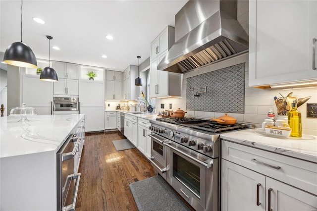 kitchen with dark wood finished floors, stainless steel appliances, a sink, wall chimney range hood, and light stone countertops