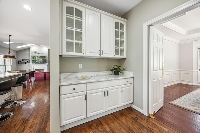 bar featuring crown molding, dark wood-type flooring, a fireplace, a ceiling fan, and pendant lighting