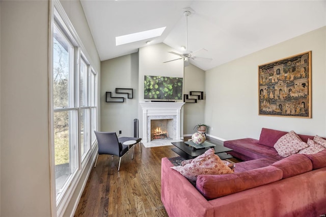 living area featuring dark wood-style floors, a fireplace, lofted ceiling with skylight, a ceiling fan, and baseboards