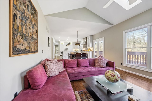 living area featuring vaulted ceiling with skylight, dark wood-style flooring, and baseboards