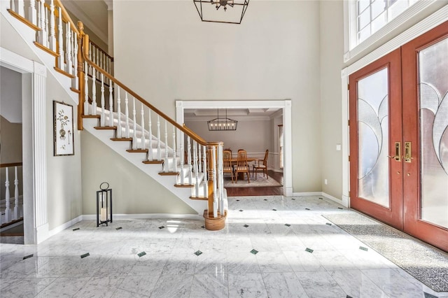 foyer with a towering ceiling, baseboards, stairs, marble finish floor, and french doors