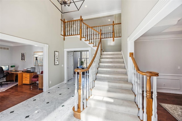 stairway with a towering ceiling, visible vents, ornamental molding, and wood finished floors