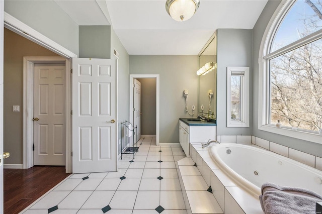 bathroom with tile patterned flooring, a healthy amount of sunlight, a jetted tub, and vanity