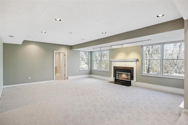 unfurnished living room featuring light carpet, a textured ceiling, baseboards, and a premium fireplace