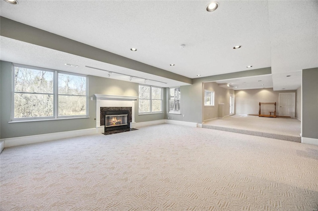 unfurnished living room with carpet floors, rail lighting, a premium fireplace, a textured ceiling, and baseboards