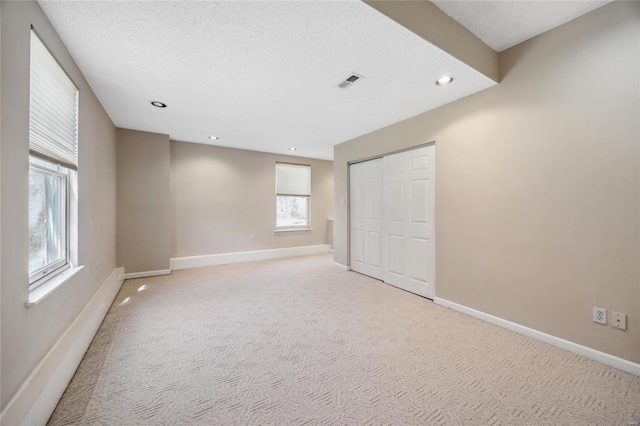 spare room featuring a textured ceiling, recessed lighting, light carpet, visible vents, and baseboards