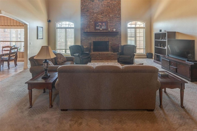 living area featuring light tile patterned floors, light colored carpet, a brick fireplace, and a high ceiling