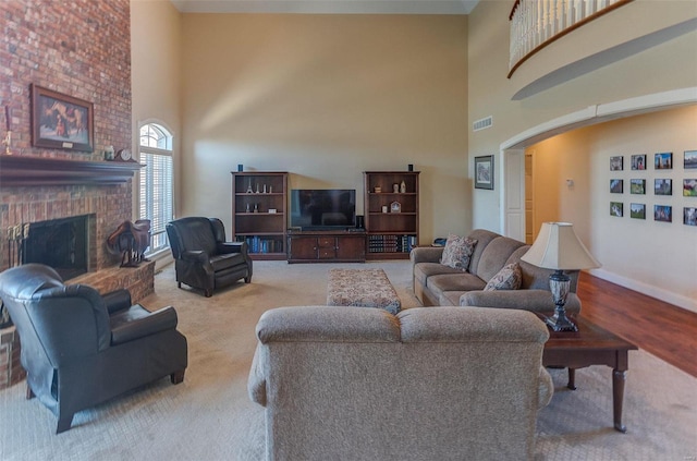 living area with visible vents, a brick fireplace, baseboards, a towering ceiling, and arched walkways