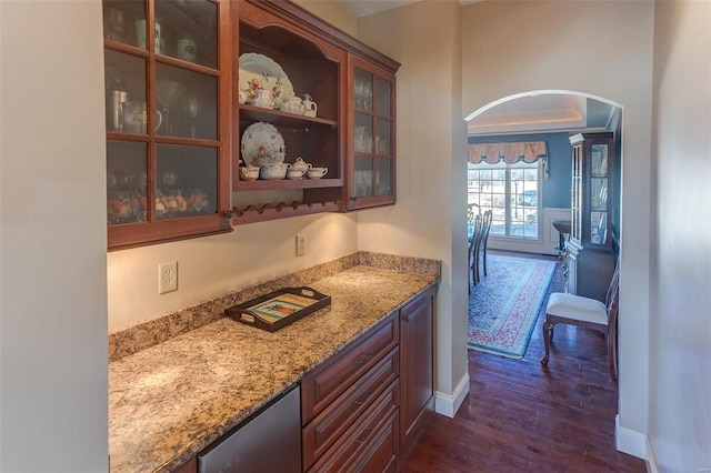 bar with baseboards, arched walkways, a bar, and dark wood-style floors