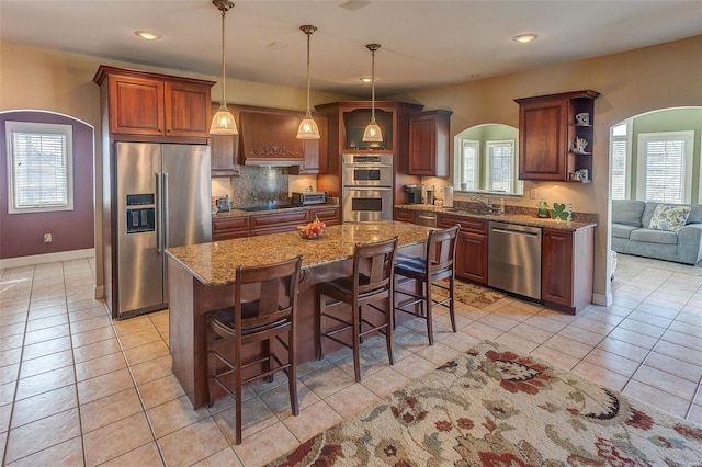 kitchen with light tile patterned floors, appliances with stainless steel finishes, a kitchen breakfast bar, arched walkways, and a sink