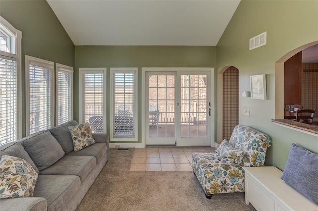 living room featuring light tile patterned floors, visible vents, high vaulted ceiling, arched walkways, and light colored carpet