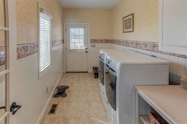 laundry area featuring washer and clothes dryer, visible vents, wainscoting, and wallpapered walls