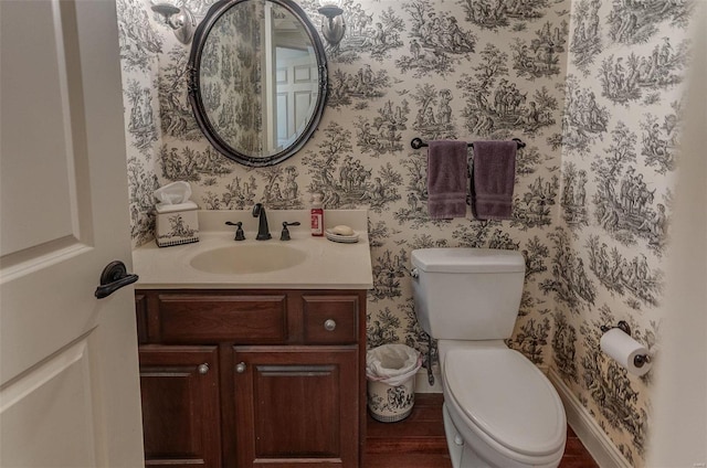 half bath with toilet, wallpapered walls, vanity, and baseboards