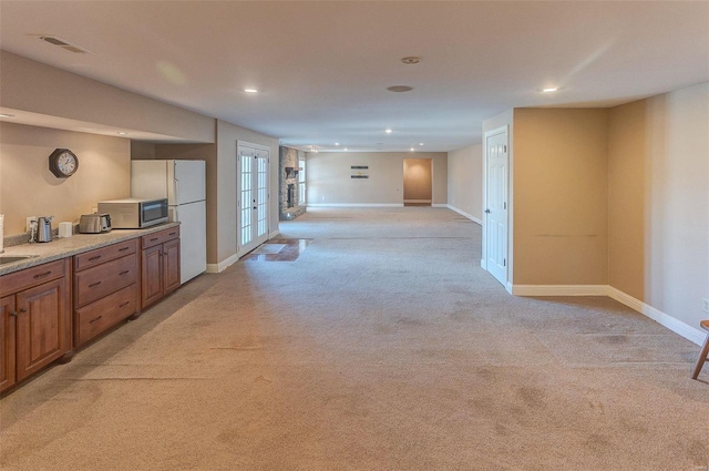 kitchen with stainless steel microwave, visible vents, baseboards, light carpet, and brown cabinets