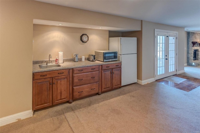 kitchen featuring brown cabinetry, a fireplace, a sink, light carpet, and stainless steel microwave