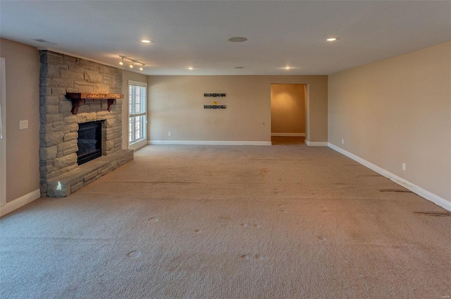 unfurnished living room featuring recessed lighting, baseboards, a stone fireplace, and light carpet