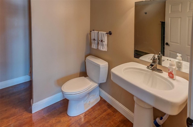 half bath featuring a sink, toilet, baseboards, and wood finished floors