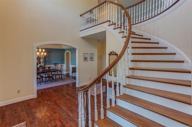 staircase with baseboards, a high ceiling, wood finished floors, and arched walkways