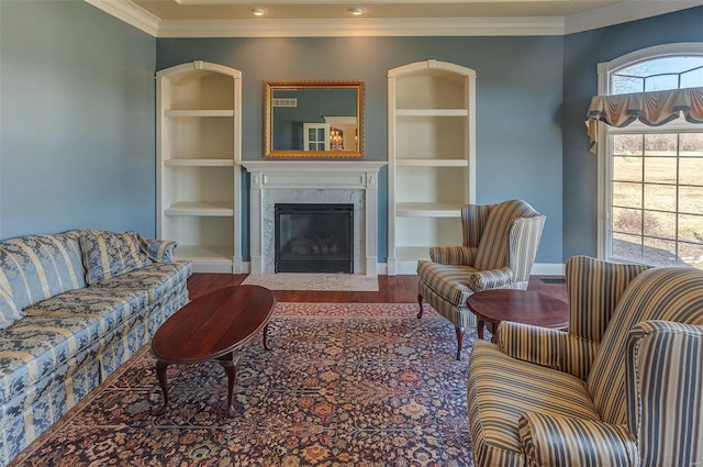 living area featuring crown molding, wood finished floors, a fireplace, and built in shelves