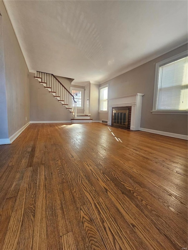 unfurnished living room featuring a fireplace, stairway, baseboards, and wood finished floors