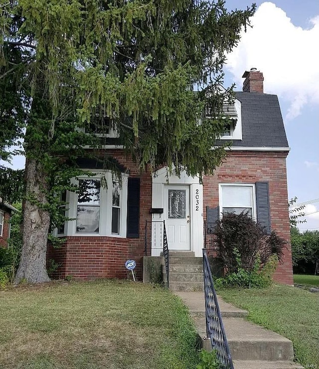 view of front of property featuring a chimney, a front lawn, and brick siding