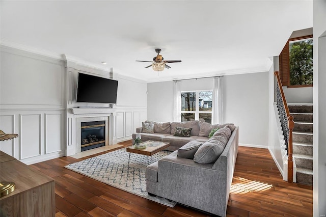 living area featuring dark wood-style floors, a fireplace with flush hearth, stairs, crown molding, and a decorative wall