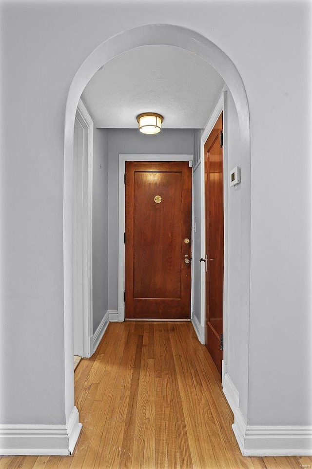 corridor with arched walkways, light wood-style flooring, and baseboards