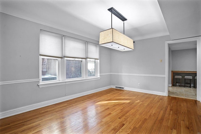 spare room with wood finished floors, visible vents, and baseboards