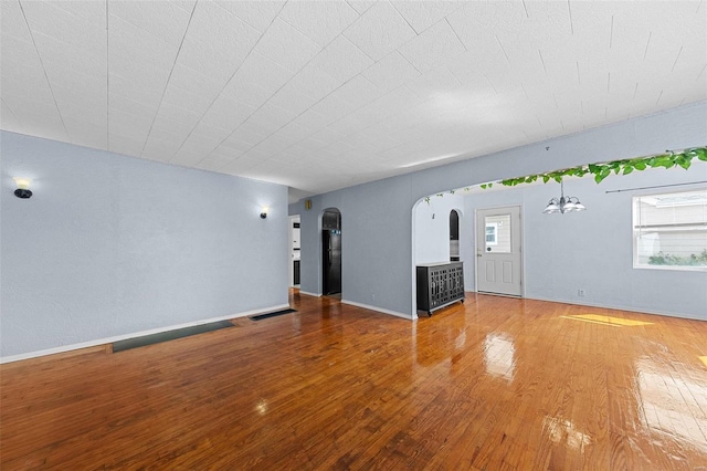 unfurnished living room featuring an inviting chandelier, baseboards, arched walkways, and wood finished floors