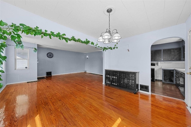 unfurnished living room with baseboards, visible vents, an inviting chandelier, and wood finished floors