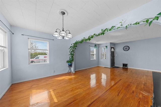 spare room with an inviting chandelier, visible vents, and wood finished floors