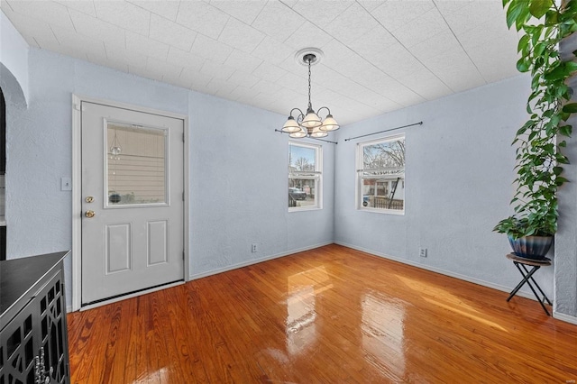 unfurnished dining area with baseboards, arched walkways, a textured wall, wood finished floors, and a chandelier