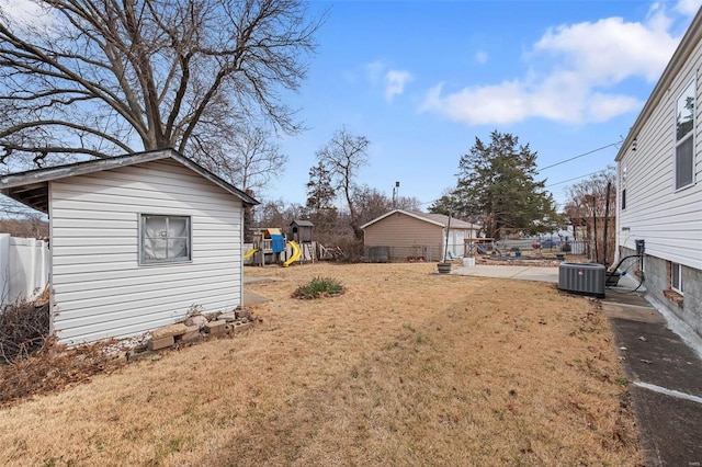 view of yard with an outbuilding, a storage unit, fence, central AC, and a playground